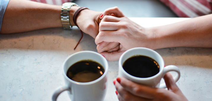 Deux personnes se tiennent la main avec deux cafés