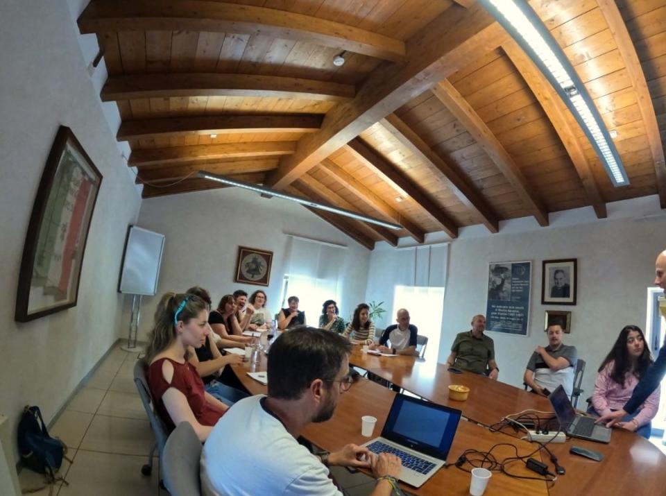 Photo d'un groupe réuni autour d'une grande table dans une salle de réunion au toît en bois et aux murs blancs