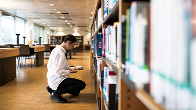 Etudiante qui cherche des conseils dans un livre à la bibliothèque